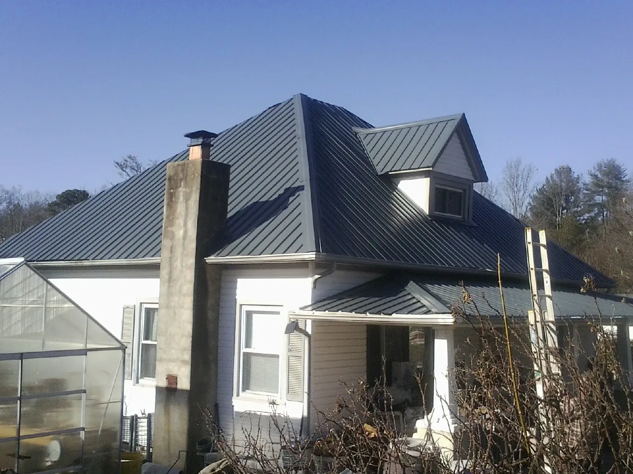 Dark blue standing seam metal roof on a white farmhouse with dormer — Slate & Tile Roof Repair by Roofing Brothers in Elkins