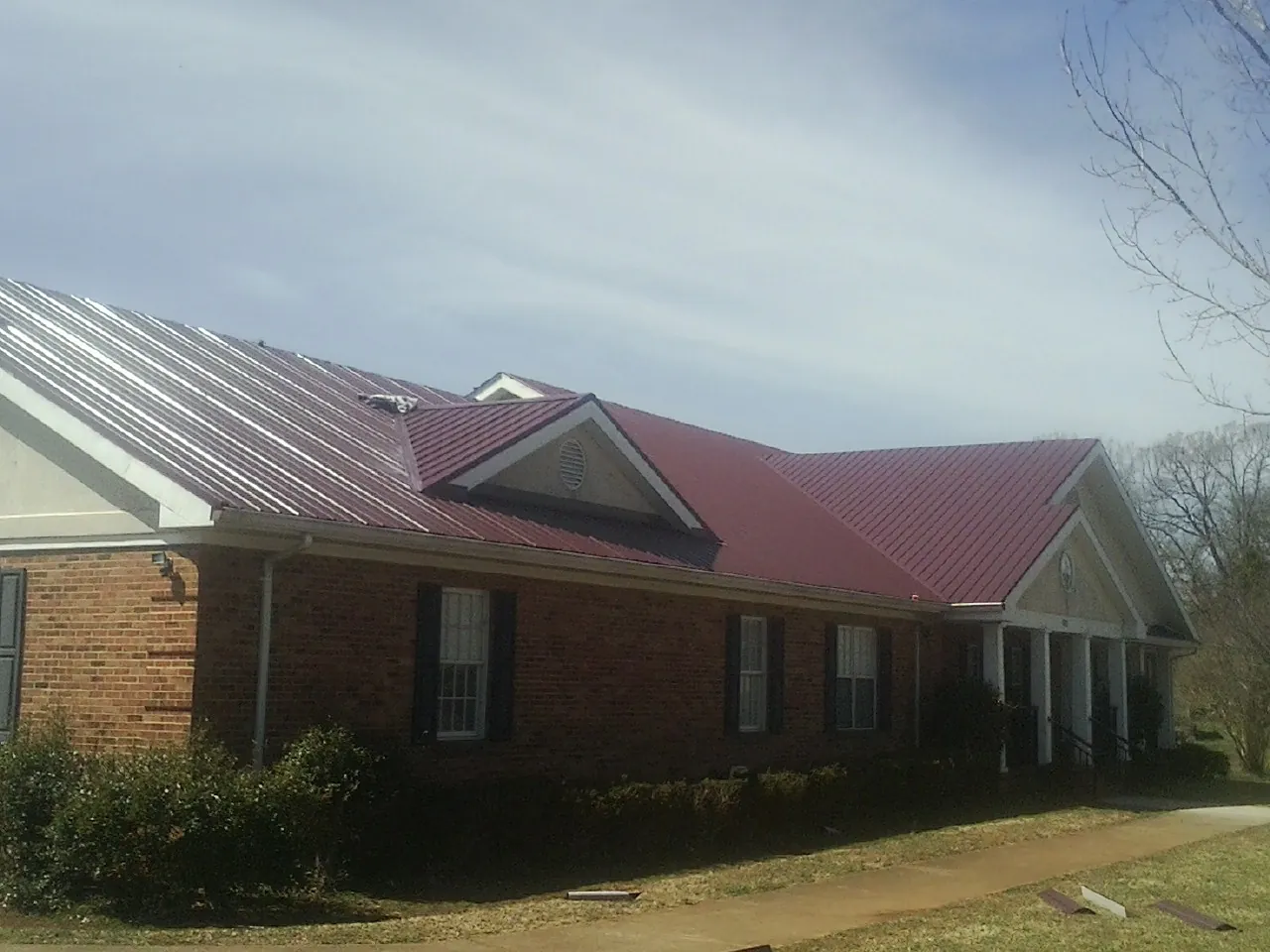 Red metal roof with gabled entries on a long brick building, from a Hail Damage Roof Repair job in Elkins
