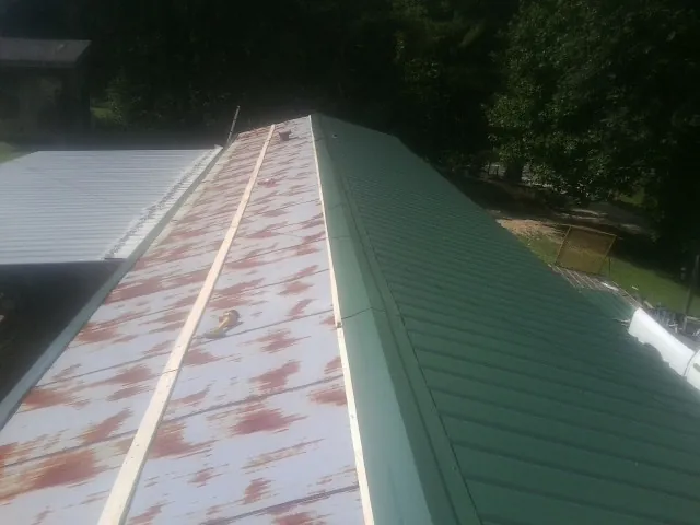 Old rusted panels beside newly installed green metal roofing — Wind Damage Roof Repair by Roofing Brothers in Elkins