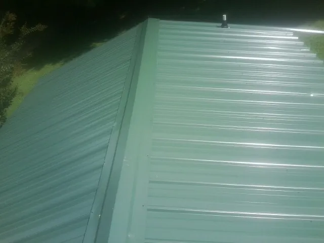 New green metal panels meeting at the ridge of a roof — Flat Roof Repair work by our crew in Elkins
