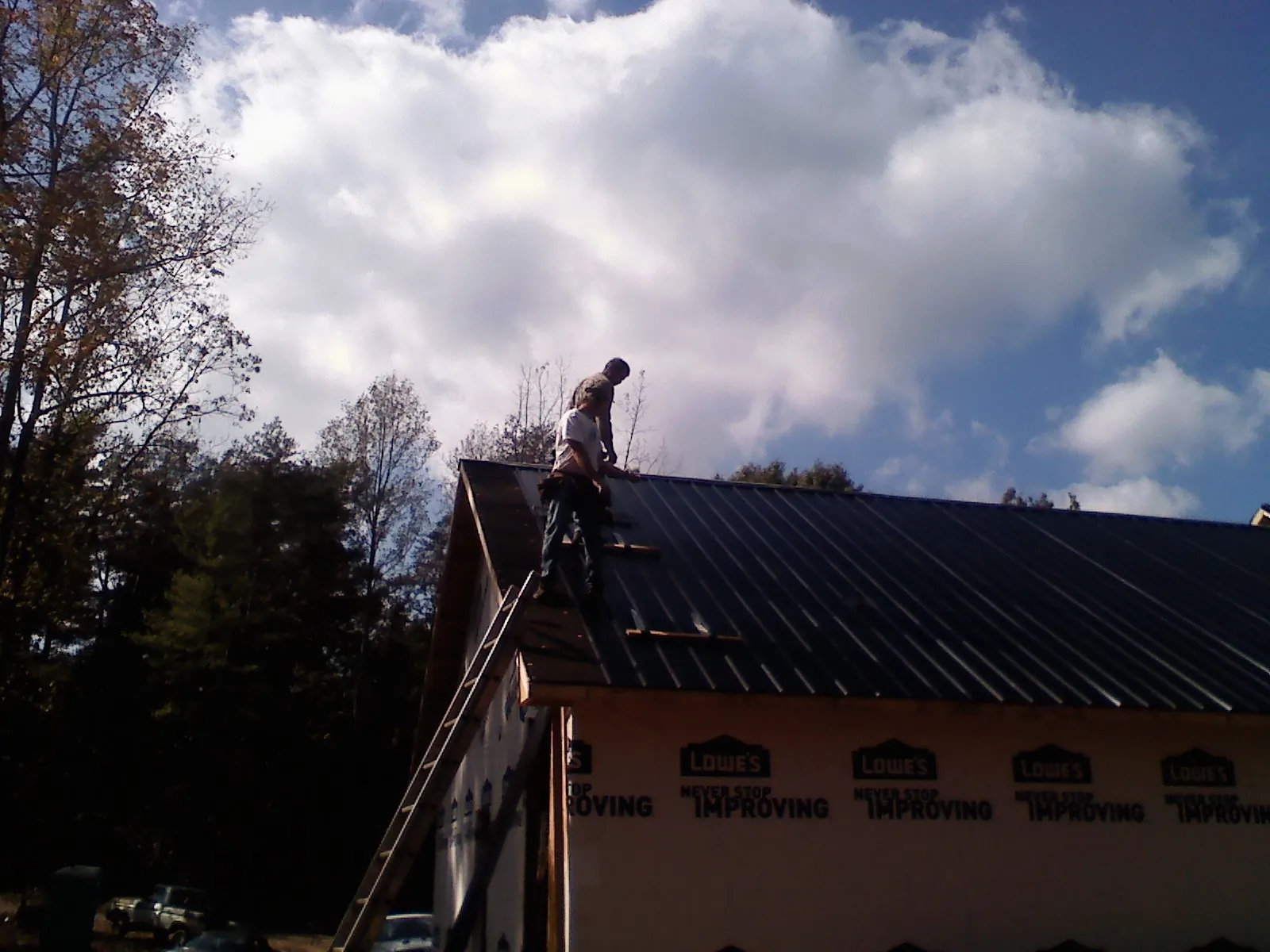 Roofer fastening dark metal panels high against a cloudy sky, from a Roof Inspection job in Elkins