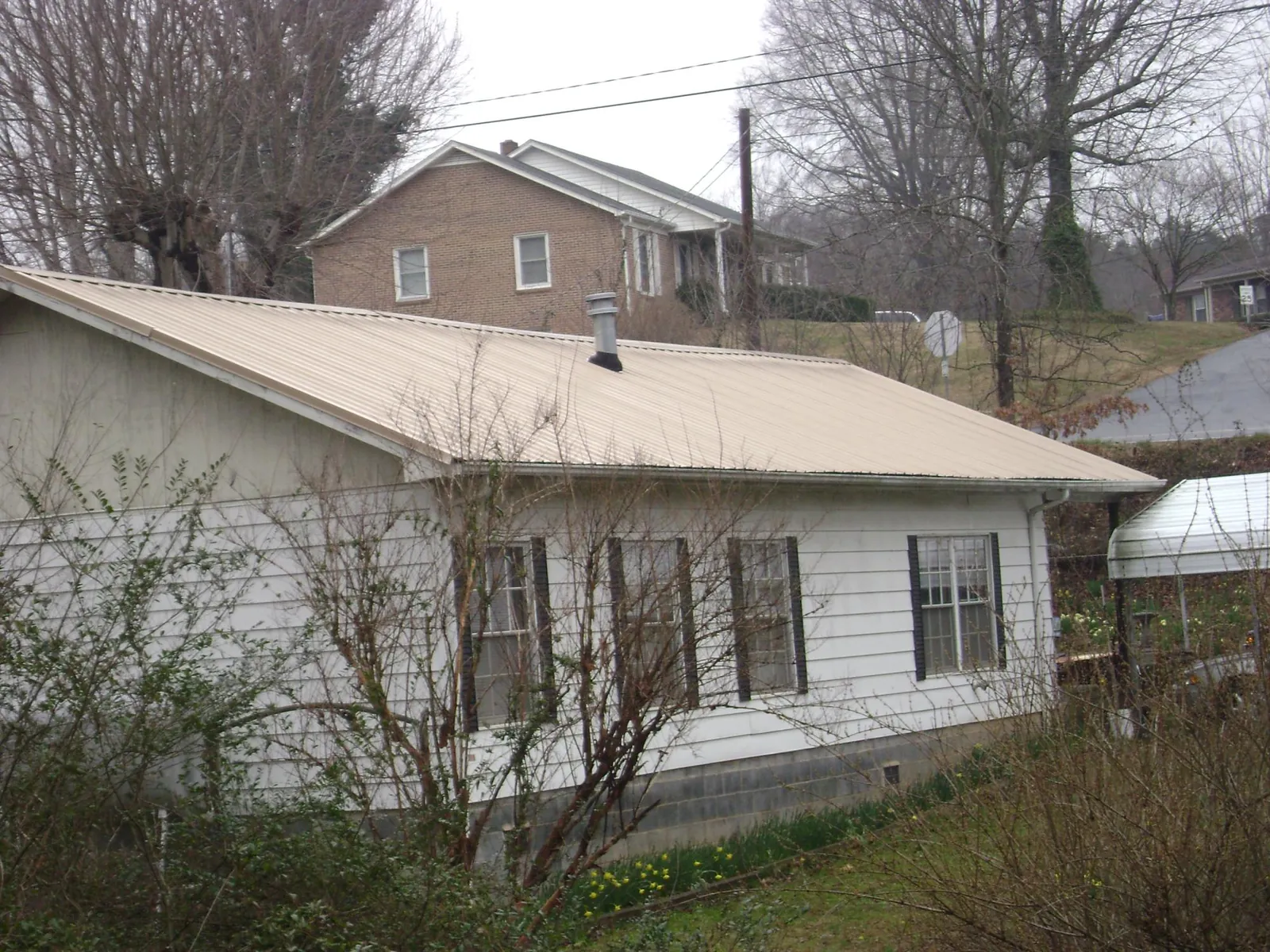 Tan metal roof on a white sided house set into a hillside — Commercial Roofing by Roofing Brothers in Elkins
