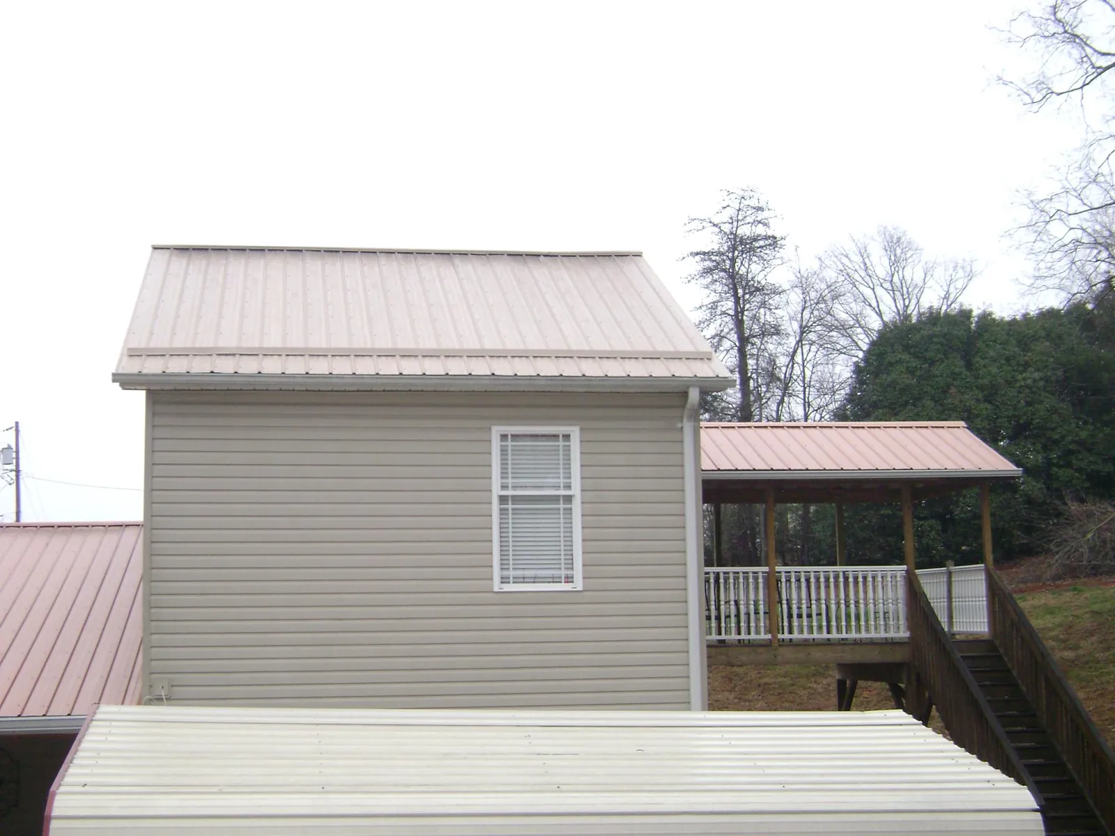 Tan metal roofs on a two story addition and attached porch, from a Roof Replacement job in Elkins