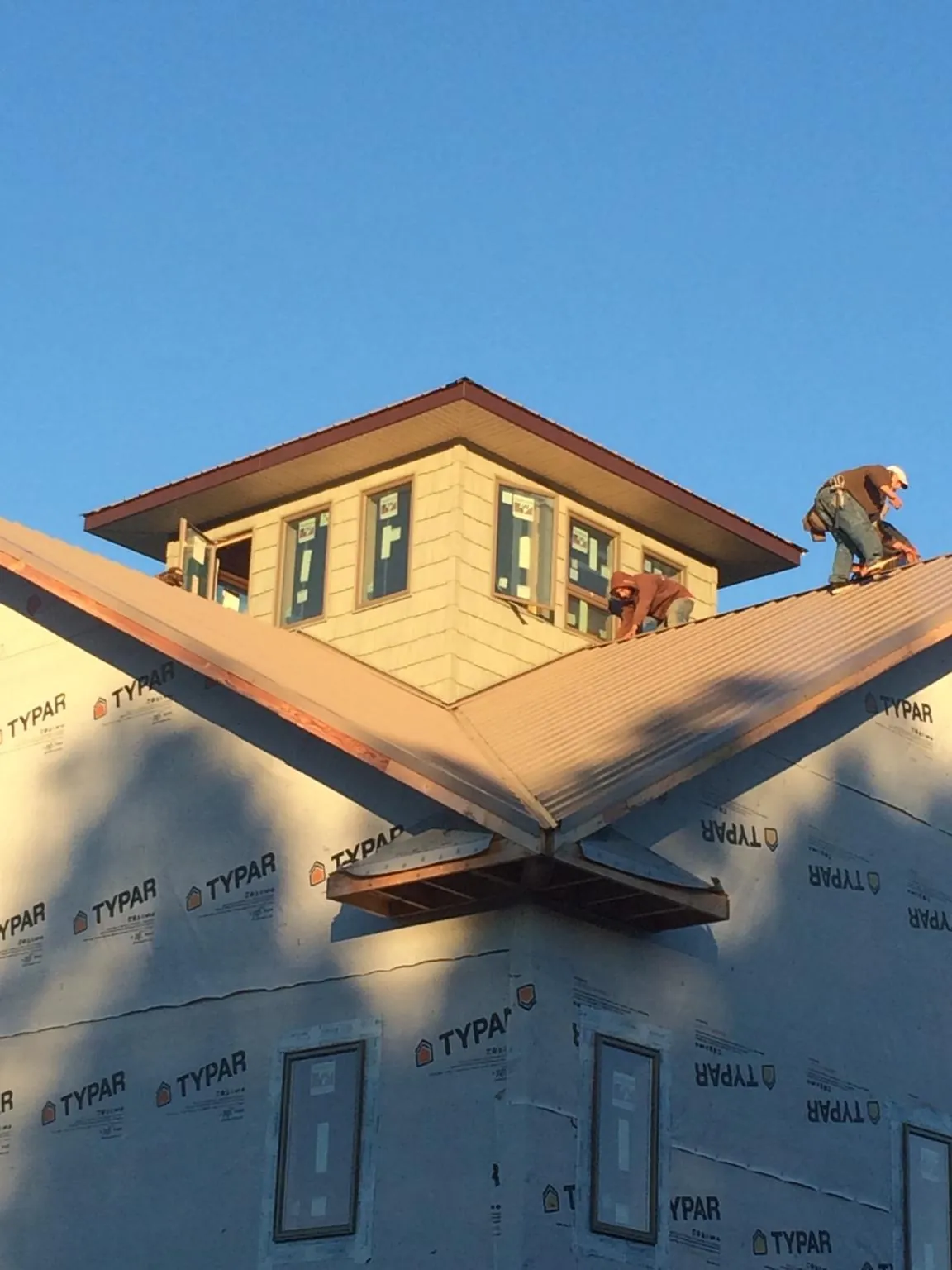 Roofers working around a rooftop cupola on a new metal roof at sunset — Roof Waterproofing in Elkins by Roofing Brothers